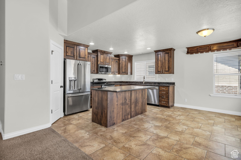 Kitchen with a textured ceiling, a kitchen island, sink, and appliances with stainless steel finishes