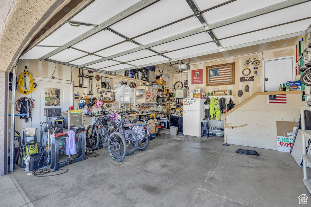 Garage with white refrigerator, a workshop area, and a garage door opener