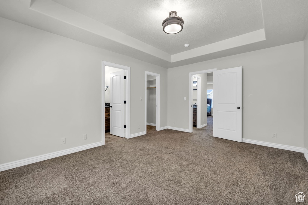 Unfurnished bedroom with a walk in closet, carpet flooring, a tray ceiling, and connected bathroom