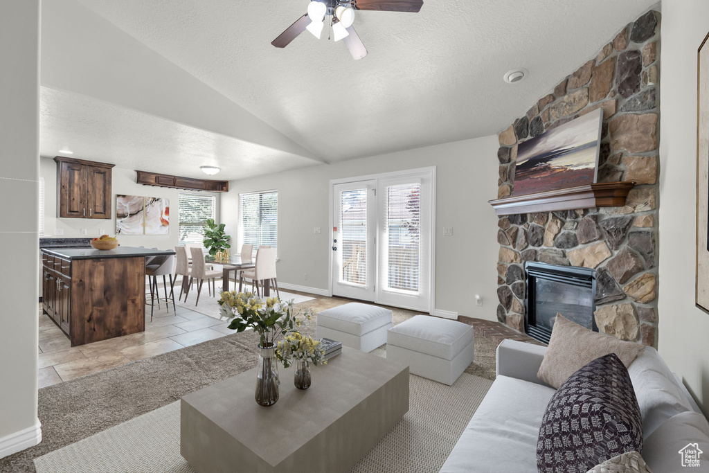 Living room with lofted ceiling, a wealth of natural light, ceiling fan, and a stone fireplace