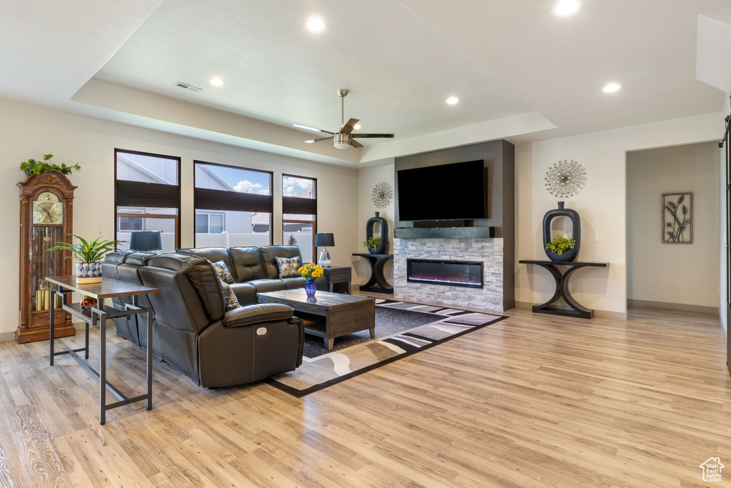 Living room featuring ceiling fan, a stone fireplace, light hardwood / wood-style flooring, and a raised ceiling