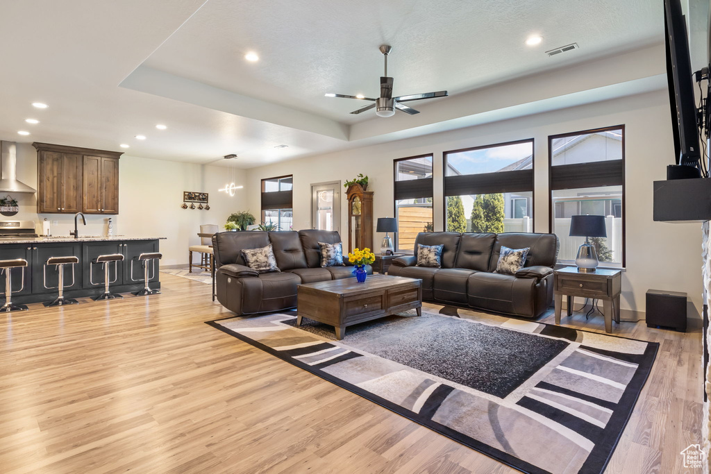 Living room featuring ceiling fan, a tray ceiling, light wood-type flooring, and sink