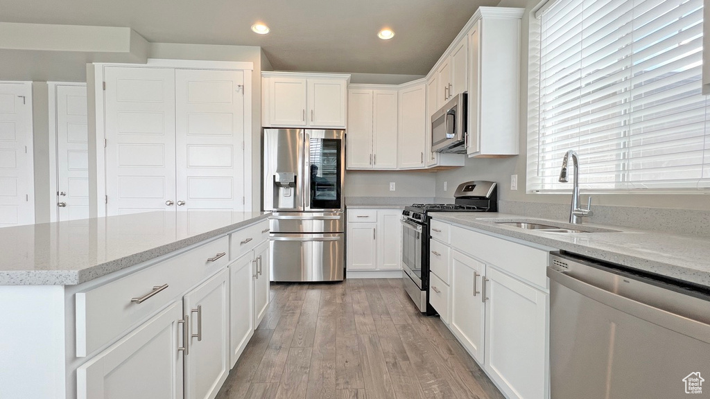 Kitchen with white cabinetry, light wood-type flooring, appliances with stainless steel finishes, light stone counters, and sink