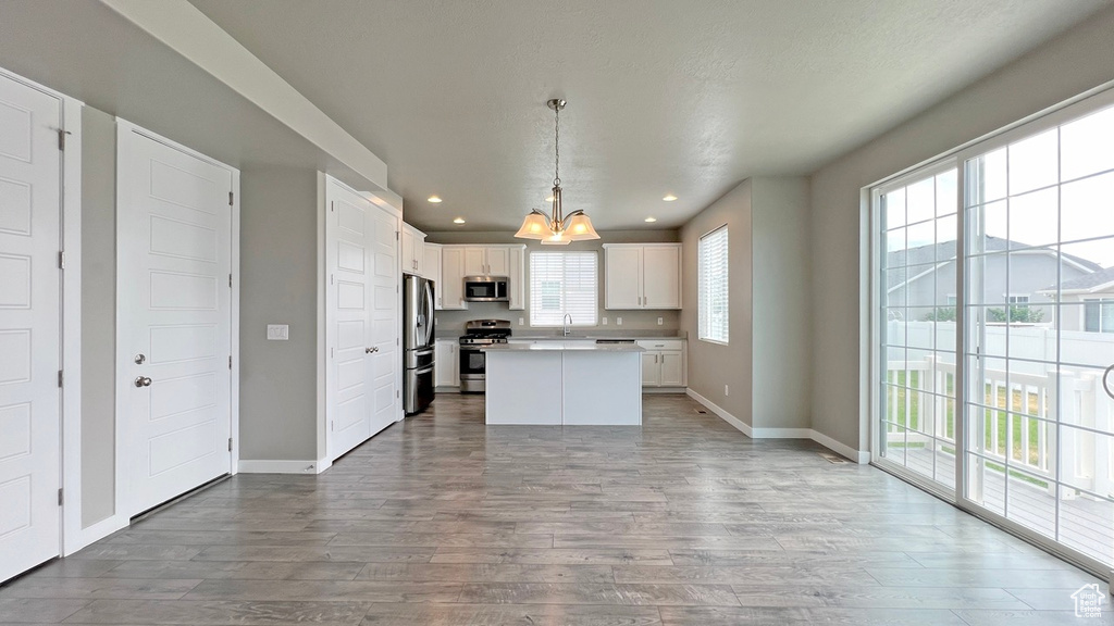 Kitchen with light hardwood / wood-style floors, hanging light fixtures, a kitchen island, appliances with stainless steel finishes, and white cabinets