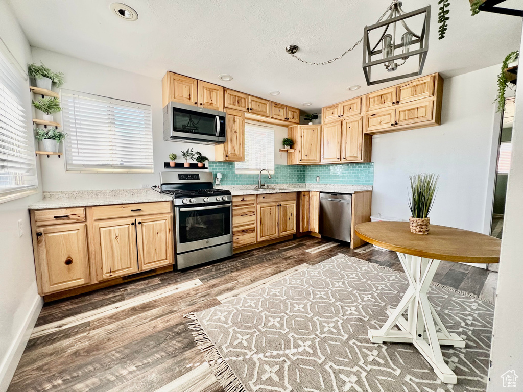 Kitchen with tasteful backsplash, dark wood-type flooring, sink, hanging light fixtures, and stainless steel appliances