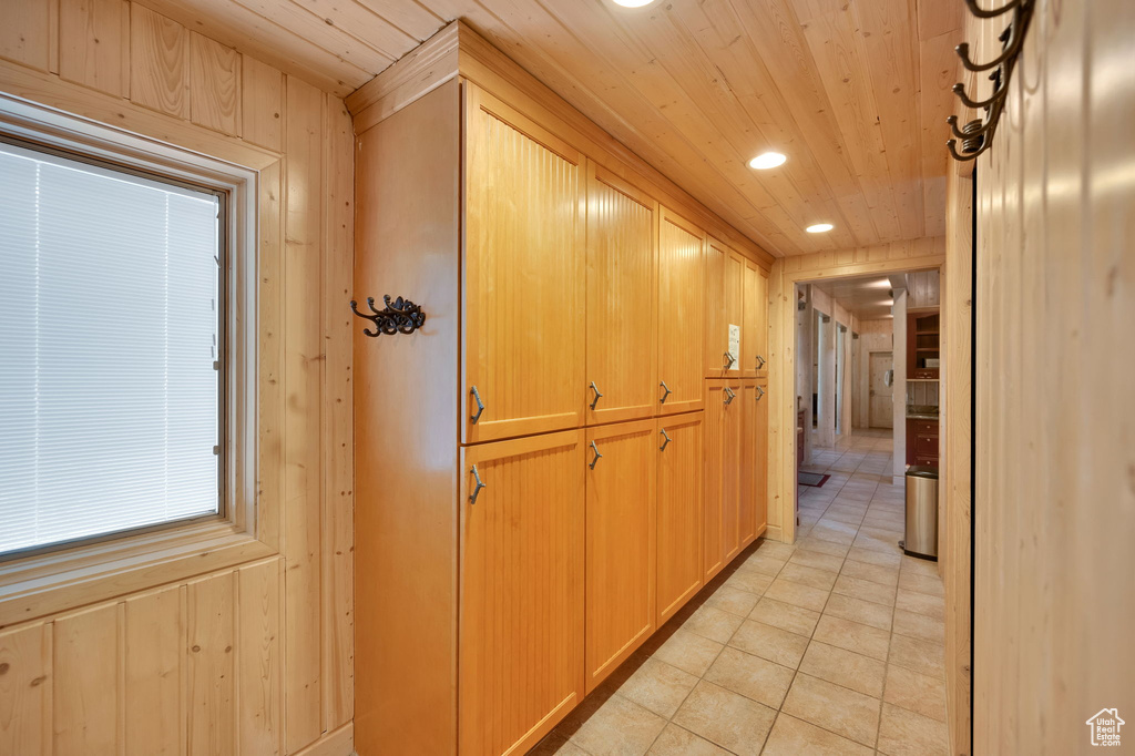 Hallway featuring light tile floors, wooden ceiling, and wood walls