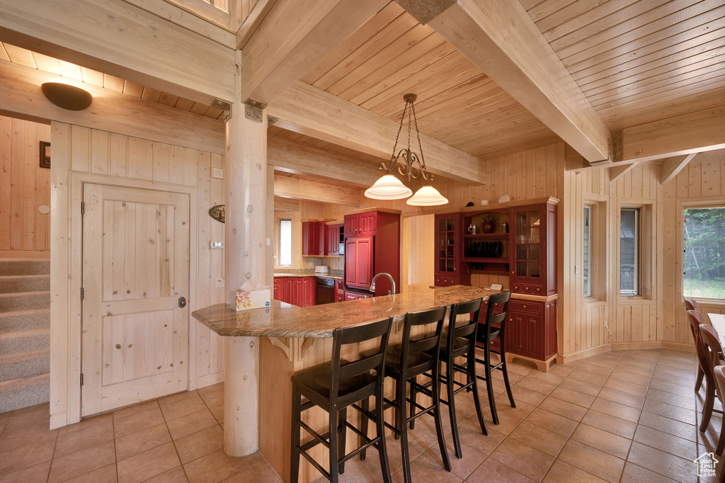 Kitchen with beamed ceiling, a breakfast bar area, decorative light fixtures, wood walls, and light tile floors