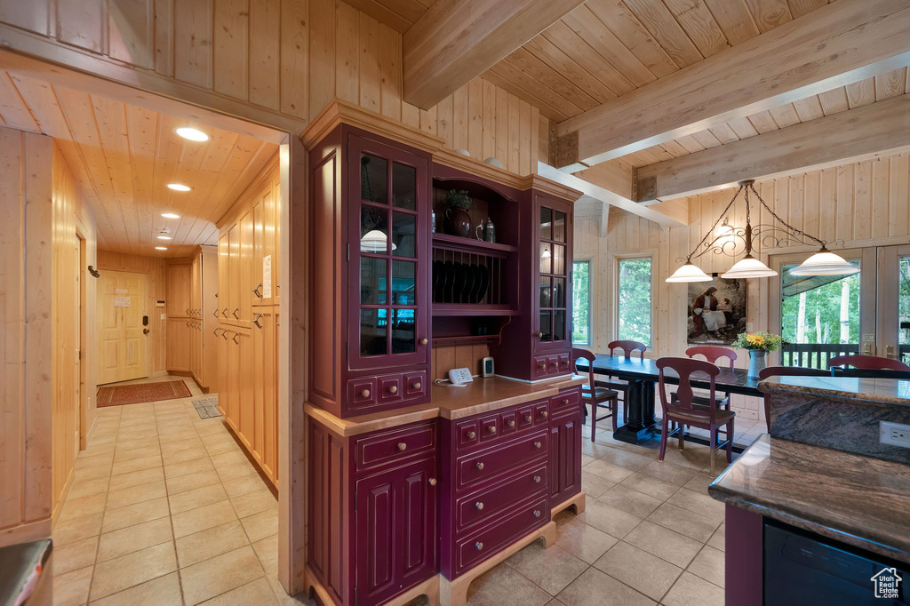 Kitchen featuring beam ceiling, hanging light fixtures, light tile flooring, and wooden walls