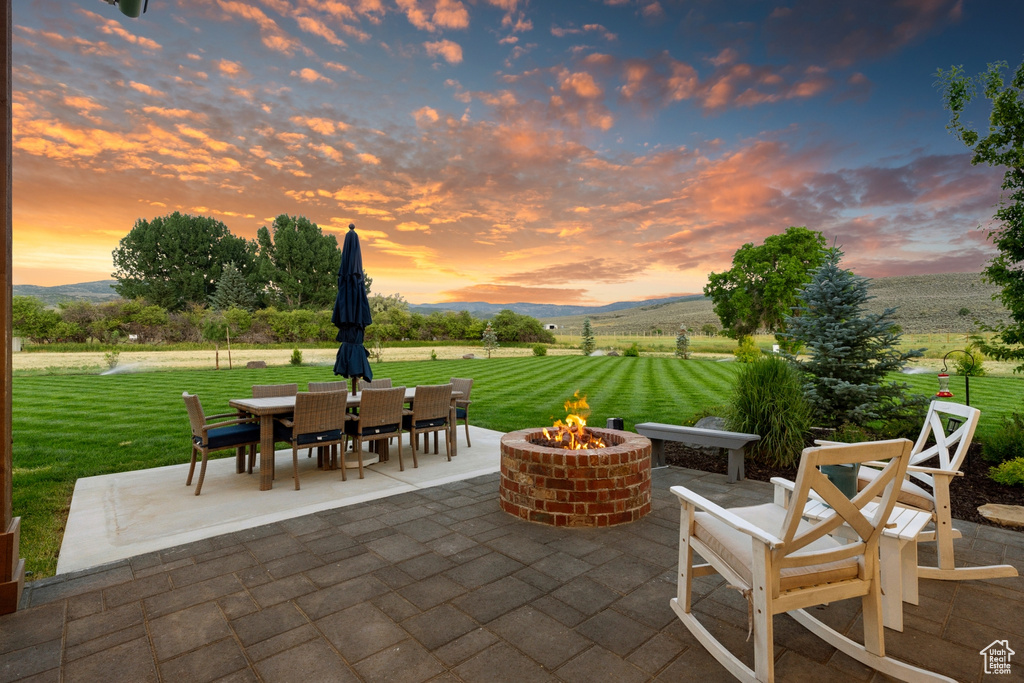 Patio terrace at dusk featuring an outdoor fire pit, a lawn, and a mountain view