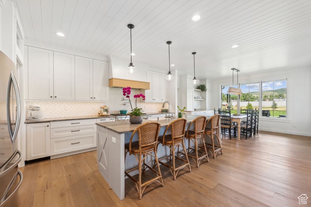 Kitchen featuring light hardwood / wood-style flooring, white cabinets, a kitchen island with sink, and backsplash