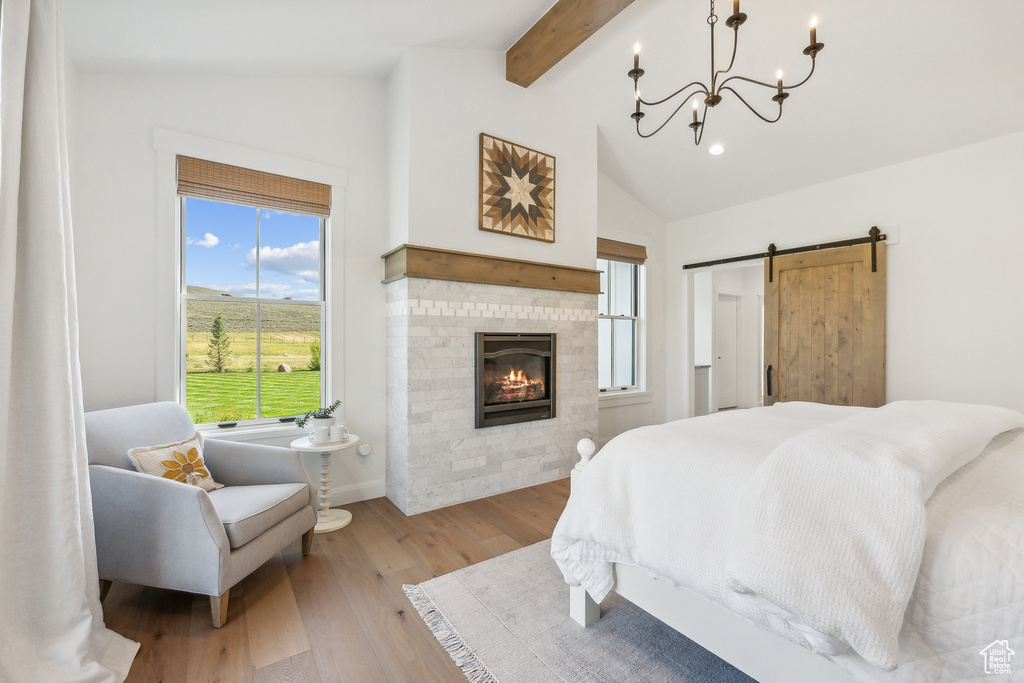 Bedroom featuring a chandelier, lofted ceiling with beams, light hardwood / wood-style floors, and a barn door