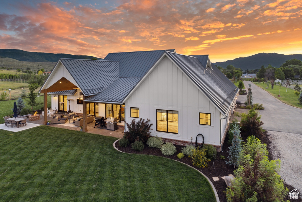 Back house at dusk featuring a mountain view, a lawn, an outdoor living space, and a patio