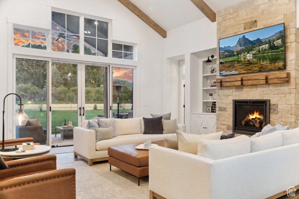 Living room featuring beamed ceiling, a healthy amount of sunlight, built in shelves, and a stone fireplace