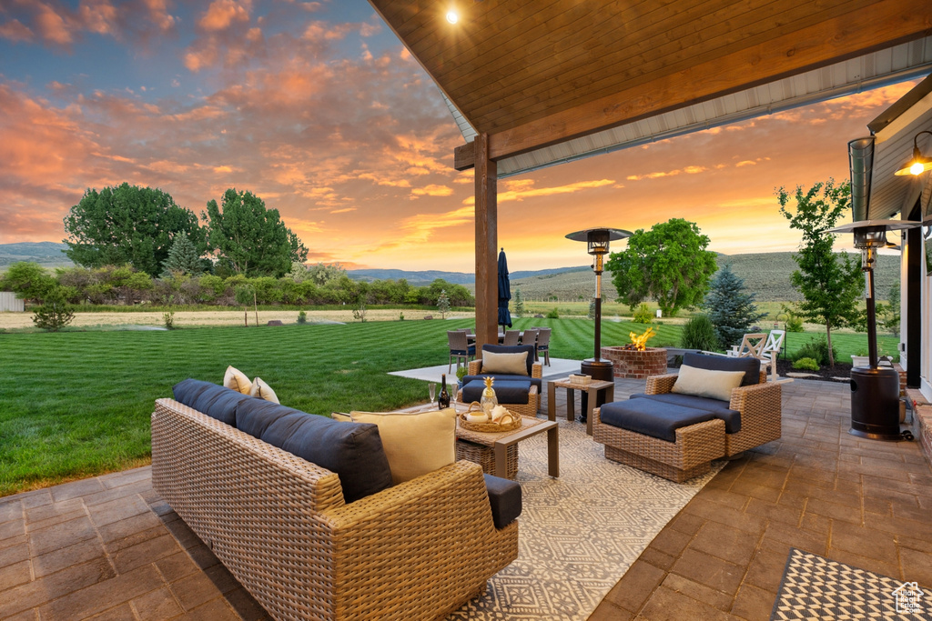 Patio terrace at dusk with an outdoor living space, a mountain view, and a yard