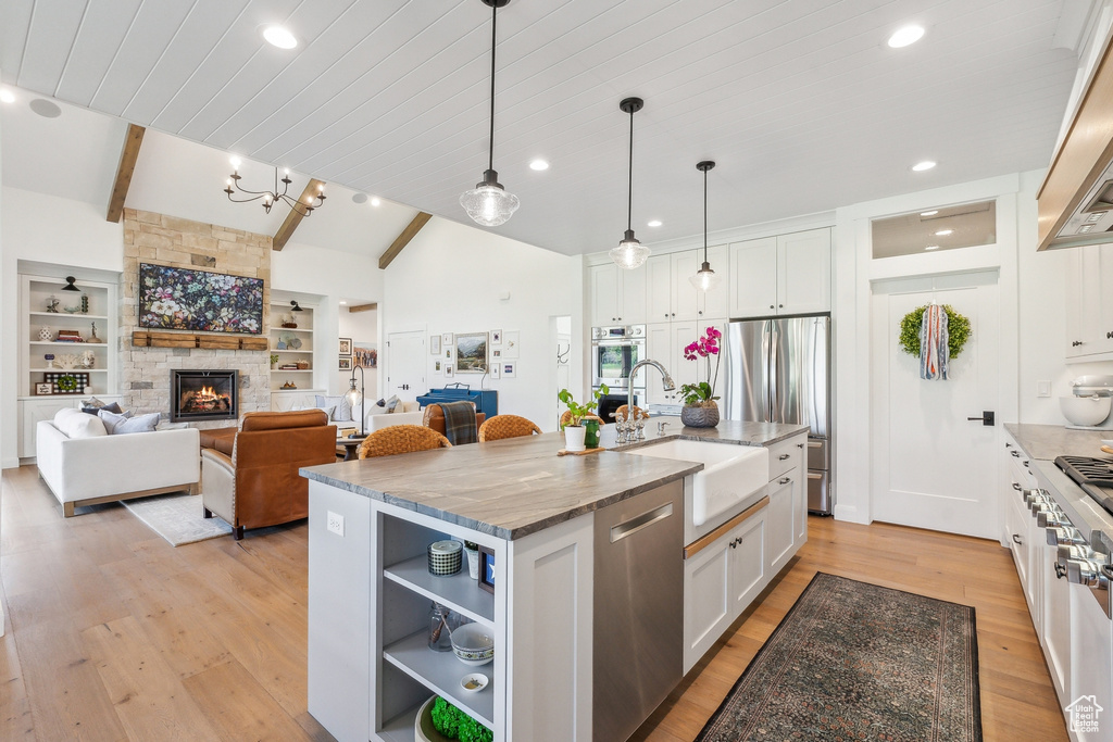 Kitchen featuring light stone countertops, light hardwood / wood-style flooring, an island with sink, white cabinetry, and appliances with stainless steel finishes