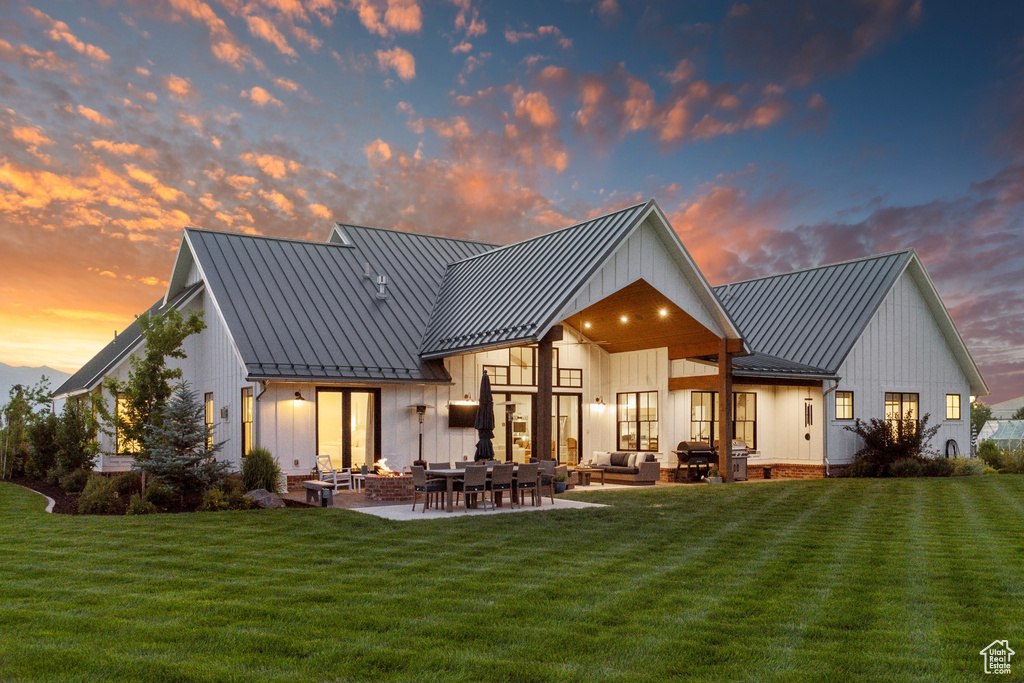 Back house at dusk featuring outdoor lounge area, a patio area, and a yard