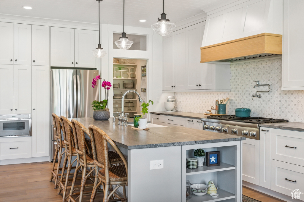 Kitchen featuring light hardwood / wood-style flooring, an island with sink, stainless steel appliances, premium range hood, and white cabinets