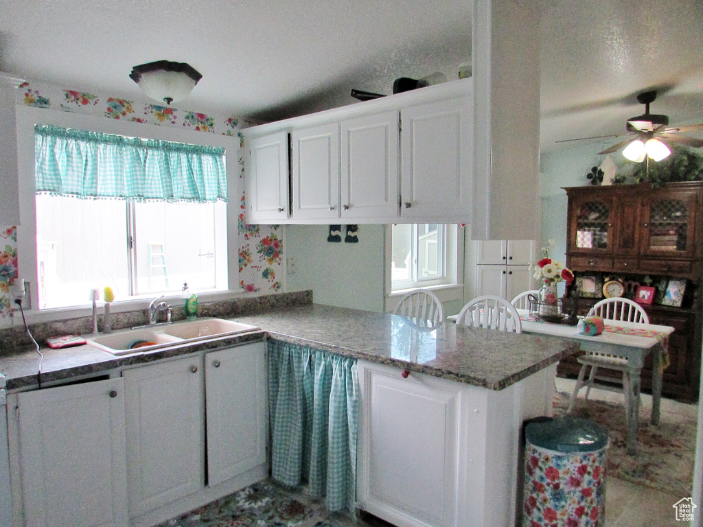 Kitchen with ceiling fan, kitchen peninsula, sink, white cabinets, and stone countertops