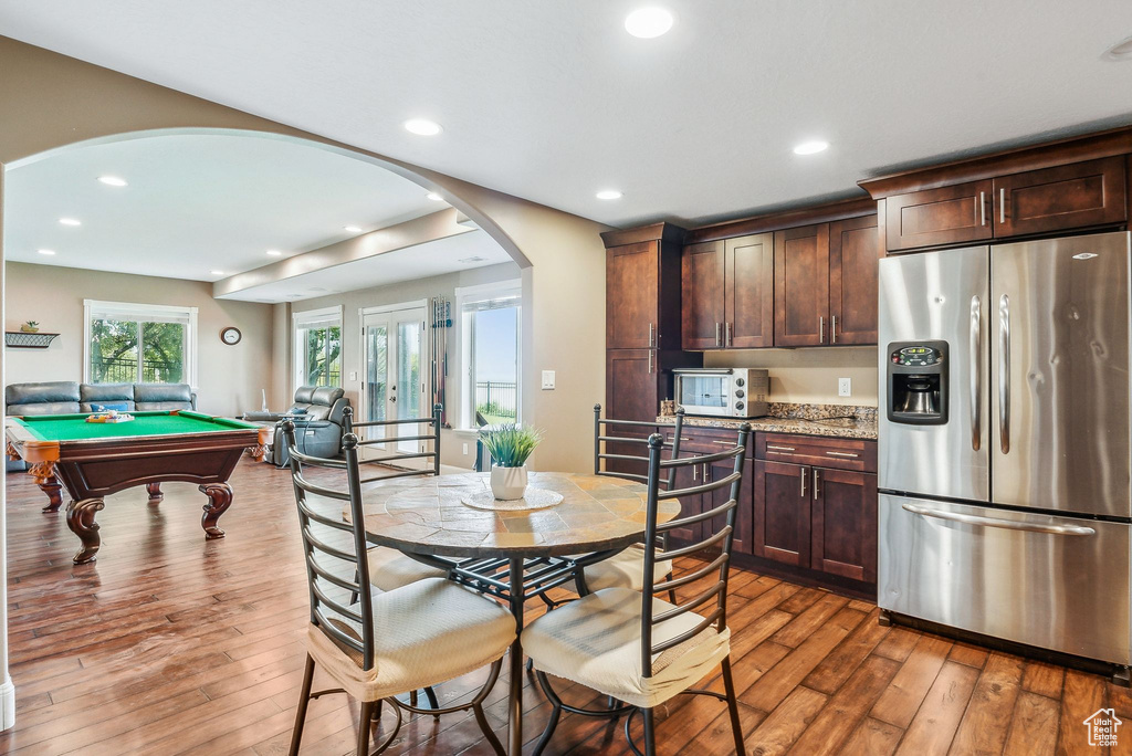 Kitchen with stainless steel fridge with ice dispenser, pool table, light stone counters, wood-type flooring, and dark brown cabinetry