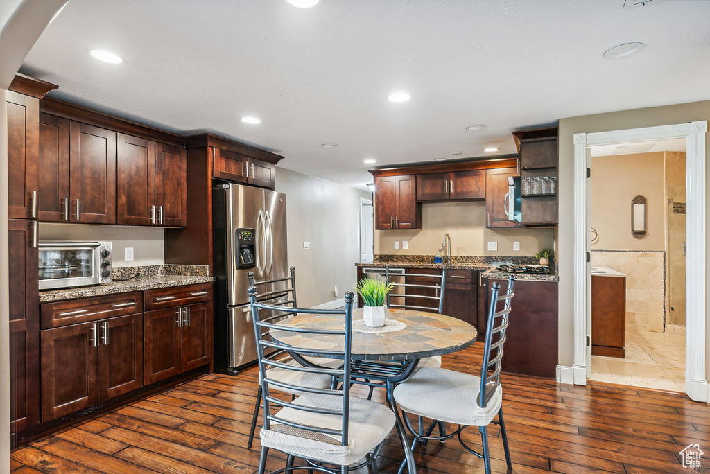 Kitchen with dark brown cabinets, stainless steel refrigerator with ice dispenser, light stone counters, and hardwood / wood-style floors