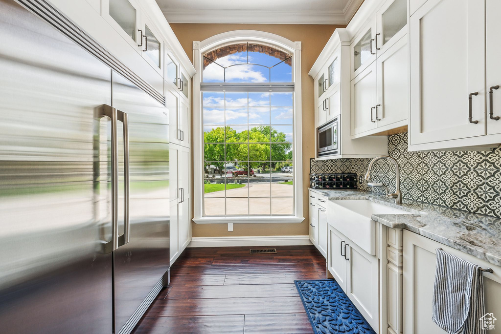 Kitchen with white cabinetry, built in appliances, dark hardwood / wood-style flooring, light stone countertops, and backsplash