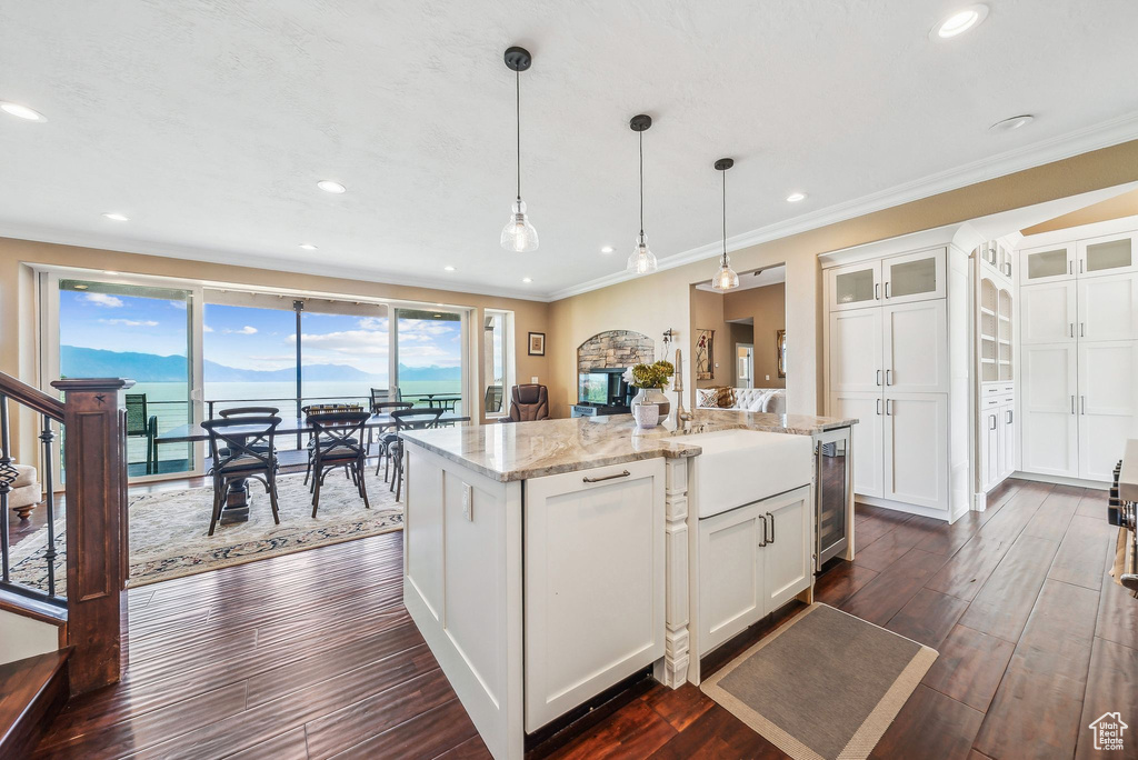 Kitchen with pendant lighting, white cabinets, ornamental molding, dark hardwood / wood-style floors, and a center island with sink