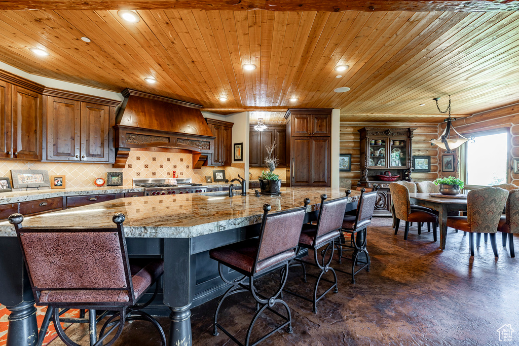 Kitchen featuring wood ceiling, a breakfast bar, a large island with sink, custom range hood, and light stone countertops