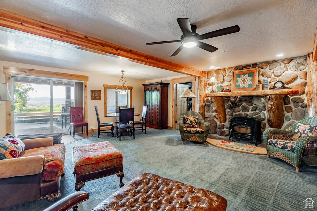 Living room with ceiling fan, beam ceiling, a fireplace, carpet flooring, and a textured ceiling