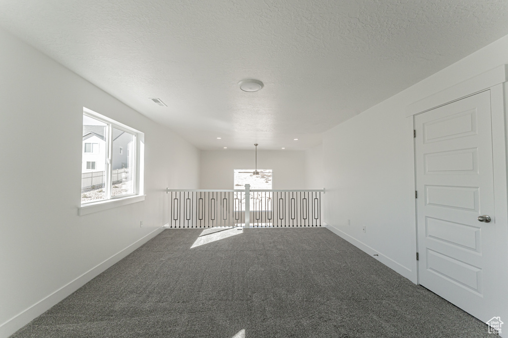 Carpeted empty room with a notable chandelier, a textured ceiling, and a wealth of natural light