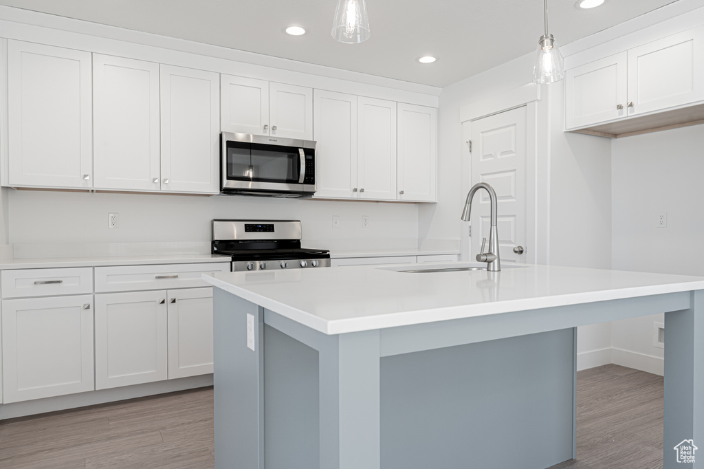 Kitchen with a kitchen island with sink, sink, white cabinets, pendant lighting, and appliances with stainless steel finishes