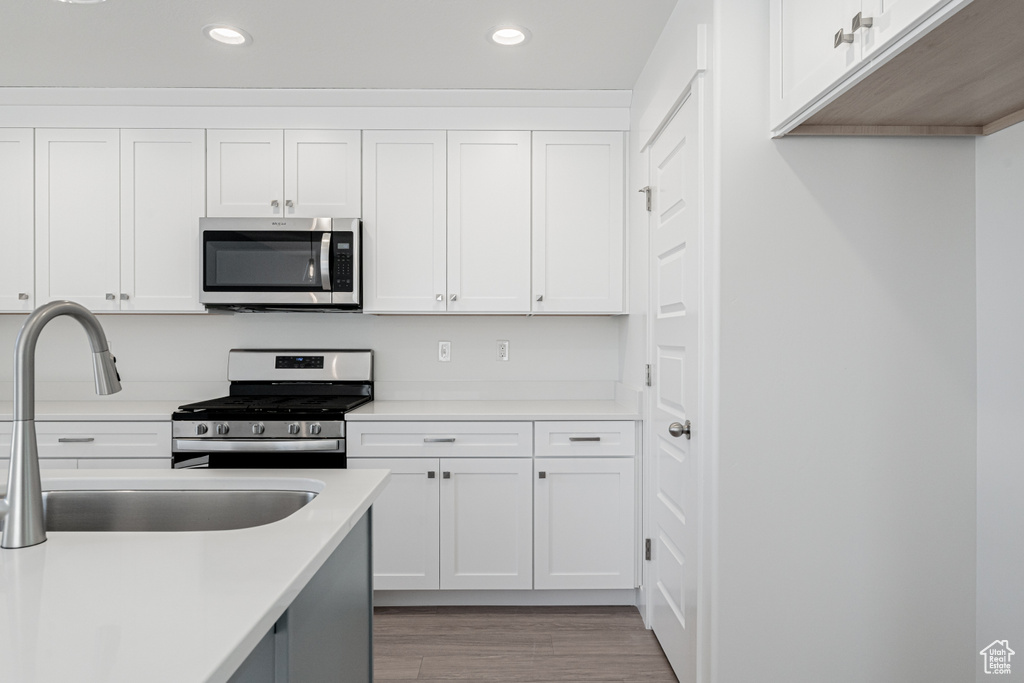 Kitchen with sink, appliances with stainless steel finishes, white cabinetry, and light hardwood / wood-style floors