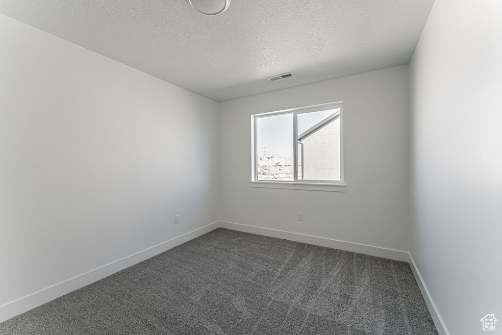 Empty room featuring a textured ceiling and dark colored carpet