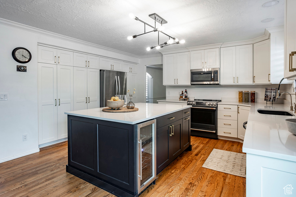 Kitchen with white cabinetry, appliances with stainless steel finishes, a center island, and light hardwood / wood-style flooring