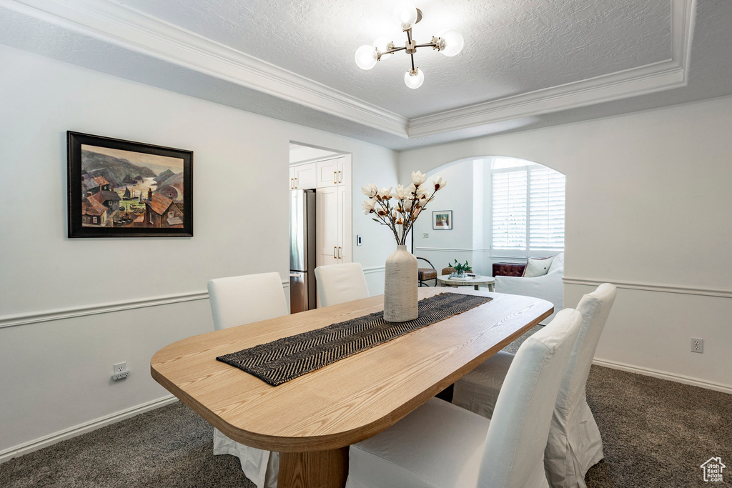 Carpeted dining area with a notable chandelier, a raised ceiling, a textured ceiling, and ornamental molding