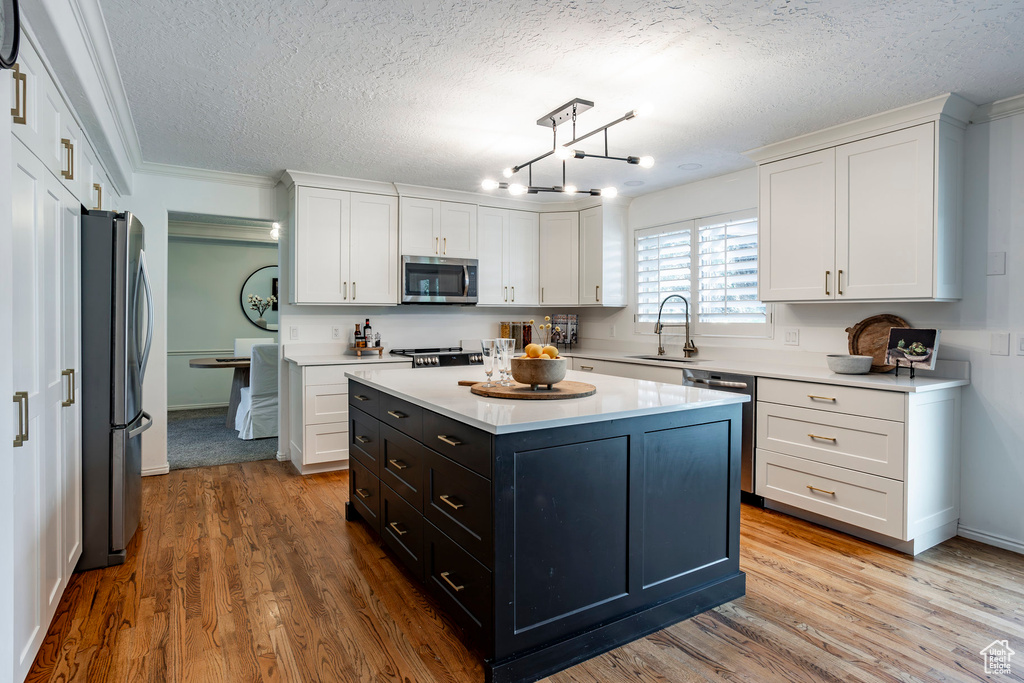 Kitchen with a center island, light hardwood / wood-style floors, white cabinetry, appliances with stainless steel finishes, and sink