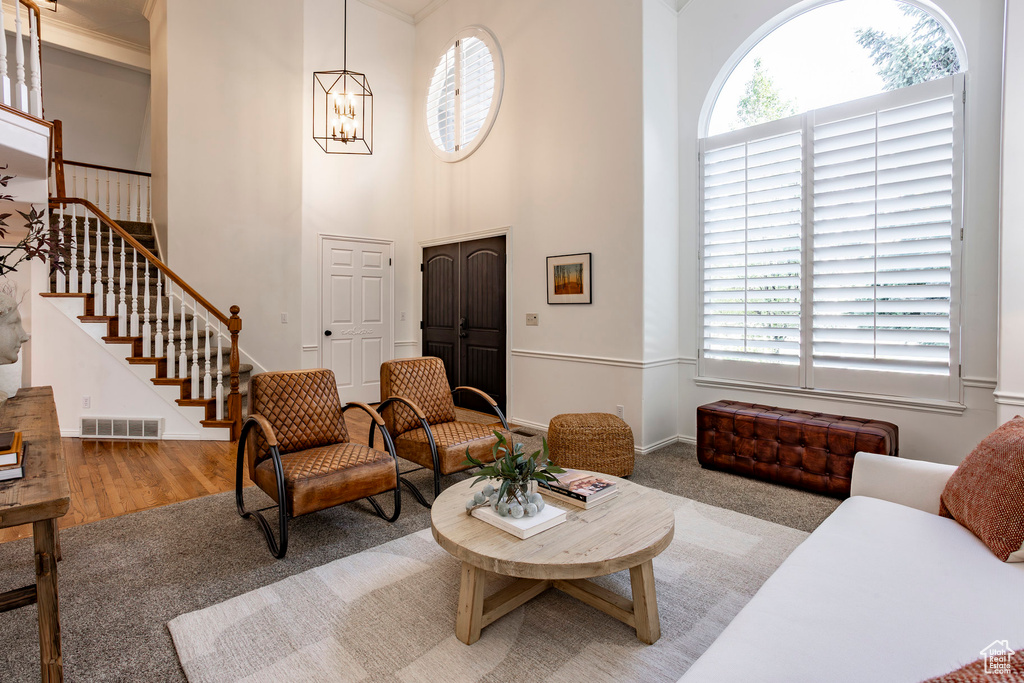 Carpeted living room featuring a towering ceiling, plenty of natural light, a chandelier, and crown molding