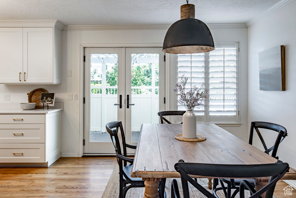 Dining room with a textured ceiling, light hardwood / wood-style floors, french doors, and crown molding