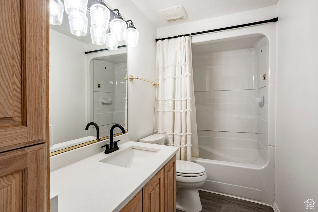 Full bathroom with wood-type flooring, shower / bath combination with curtain, vanity, and toilet