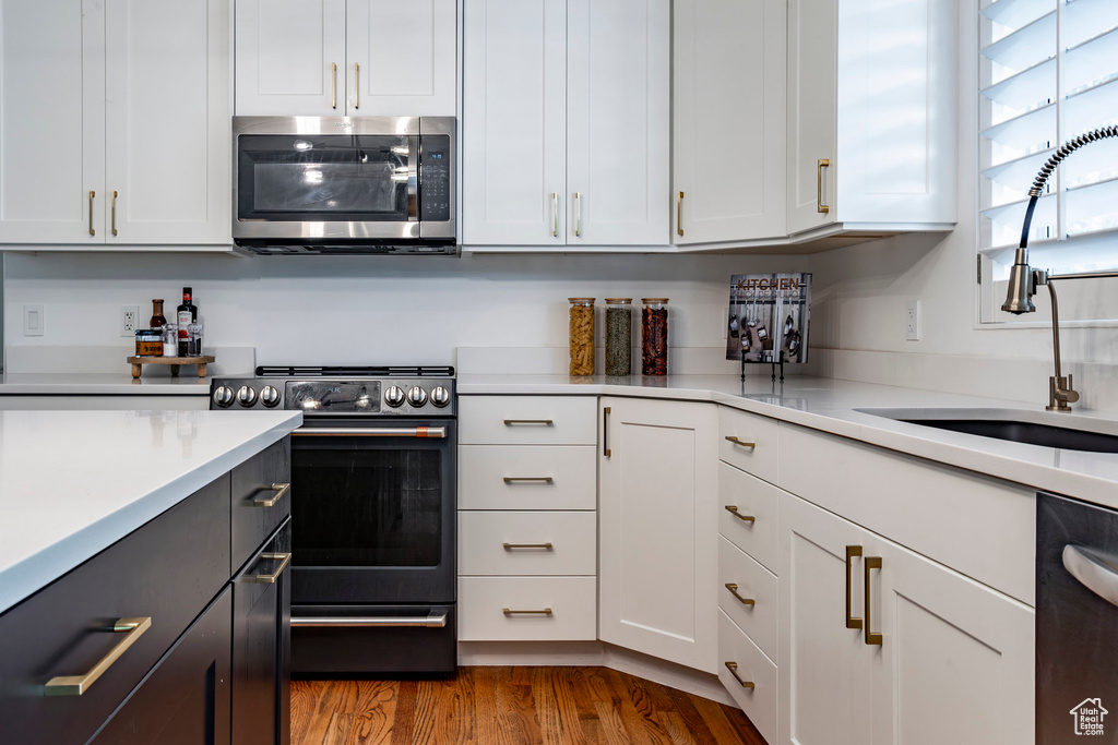 Kitchen with white cabinets, hardwood / wood-style floors, black appliances, and sink