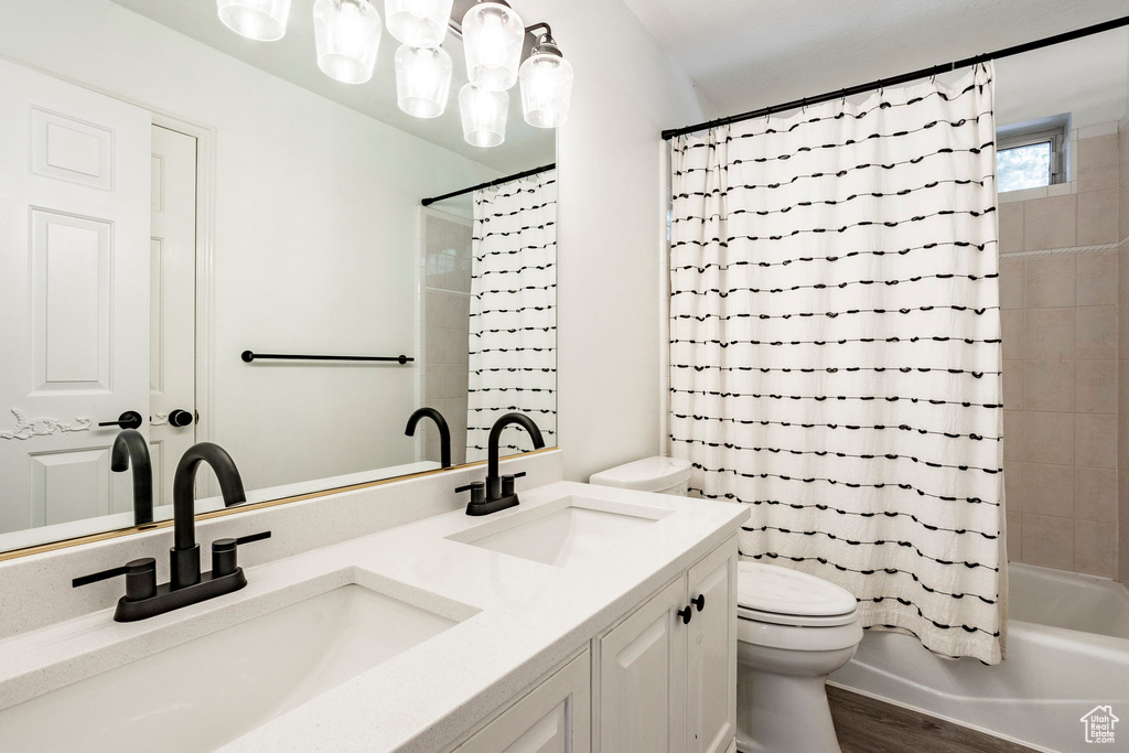 Full bathroom featuring double sink vanity, hardwood / wood-style floors, shower / bath combo with shower curtain, and toilet