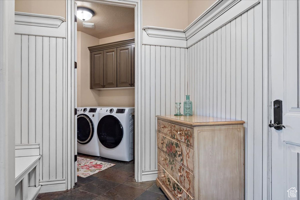 Laundry room with dark tile flooring, washing machine and clothes dryer, and cabinets