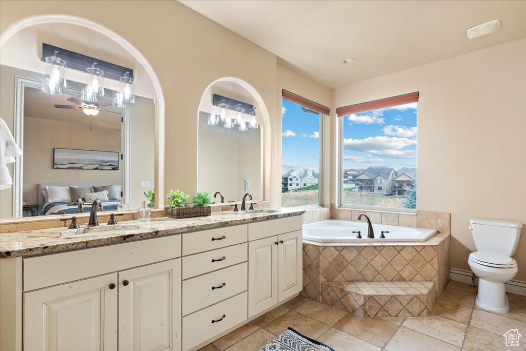 Bathroom featuring tile flooring, dual vanity, a relaxing tiled bath, ceiling fan, and toilet