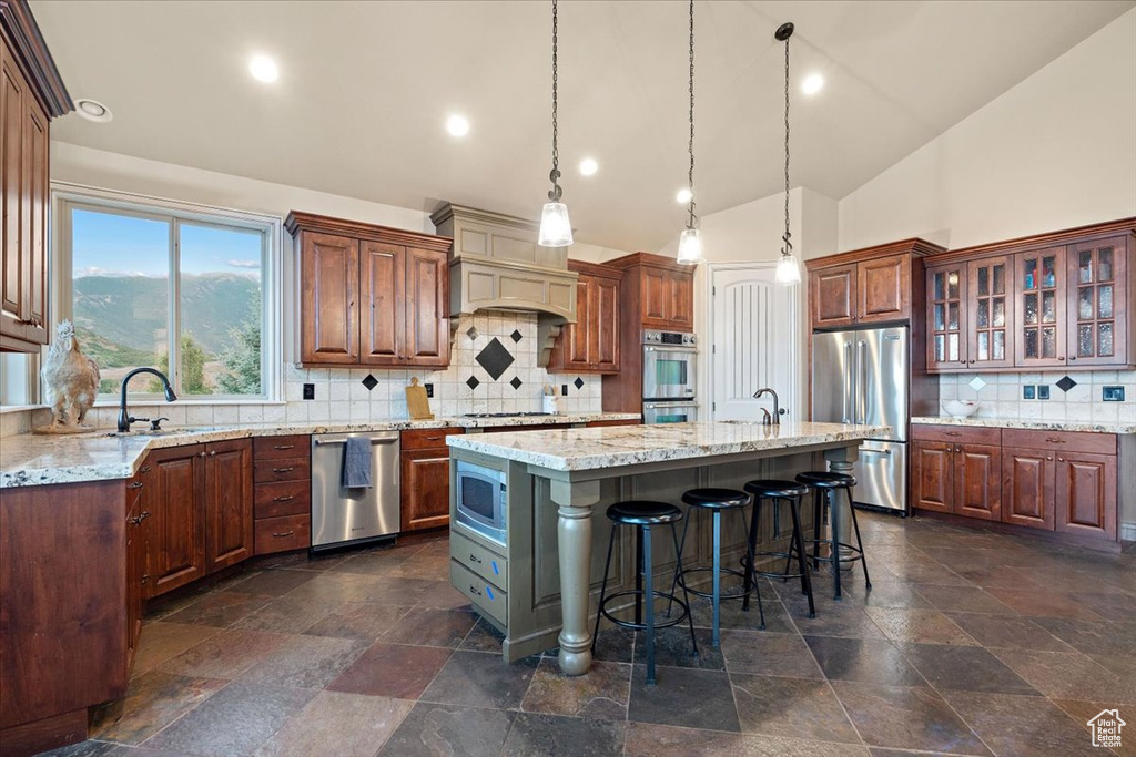 Kitchen with stainless steel appliances, hanging light fixtures, tasteful backsplash, a kitchen island with sink, and premium range hood