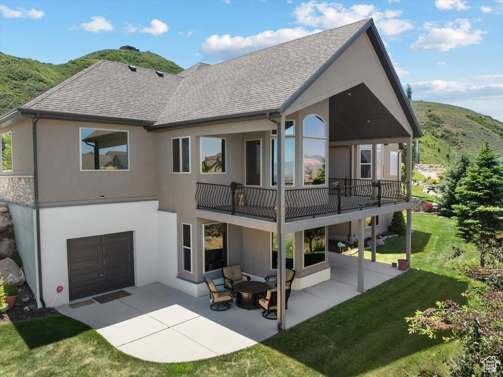 Rear view of house featuring a garage, a patio, a mountain view, a balcony, and a lawn