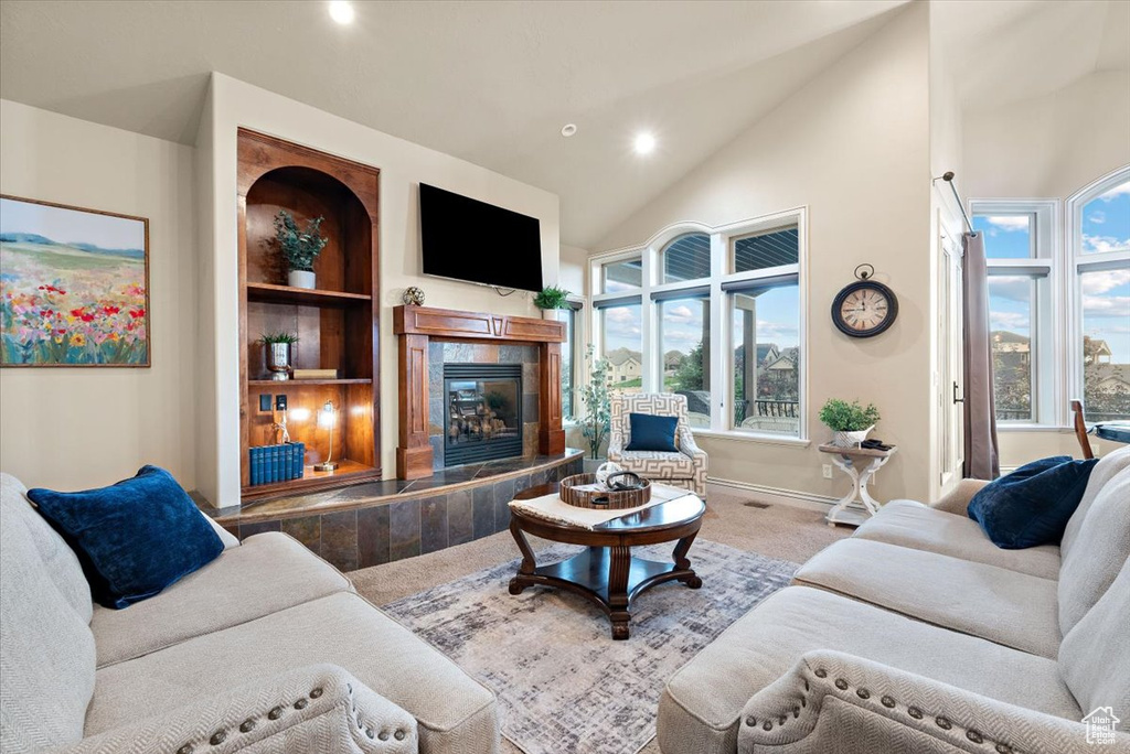 Living room with built in features, a tiled fireplace, a healthy amount of sunlight, and carpet floors