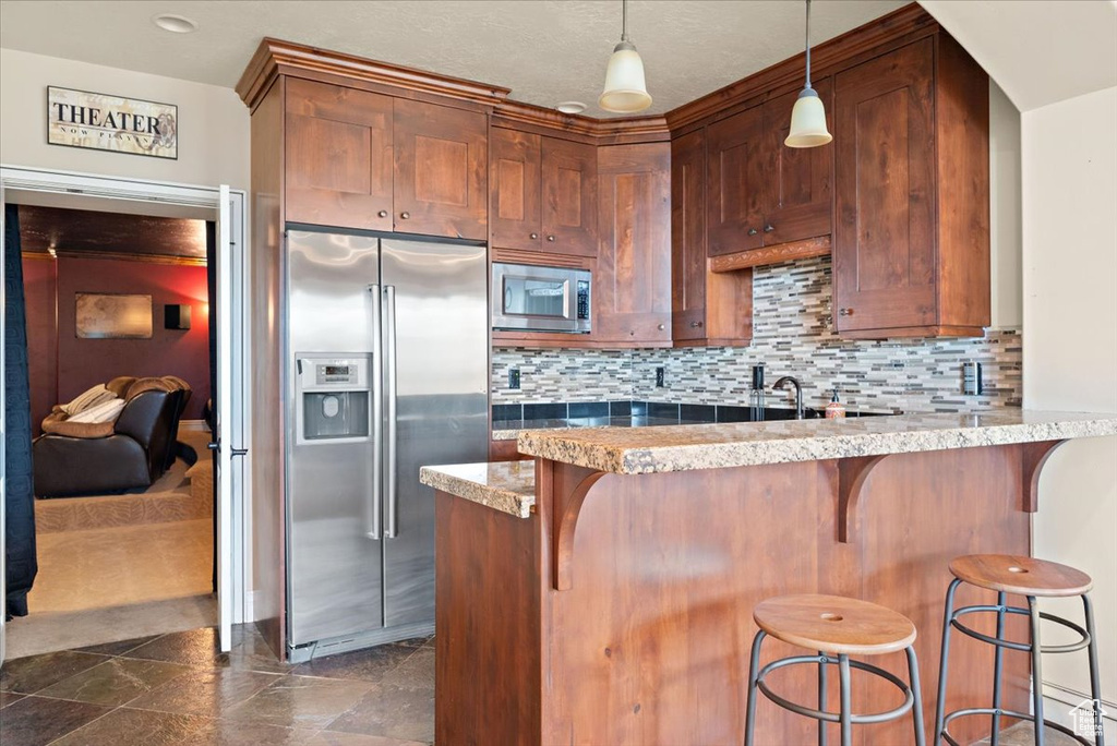 Kitchen featuring decorative light fixtures, dark tile floors, tasteful backsplash, appliances with stainless steel finishes, and a breakfast bar