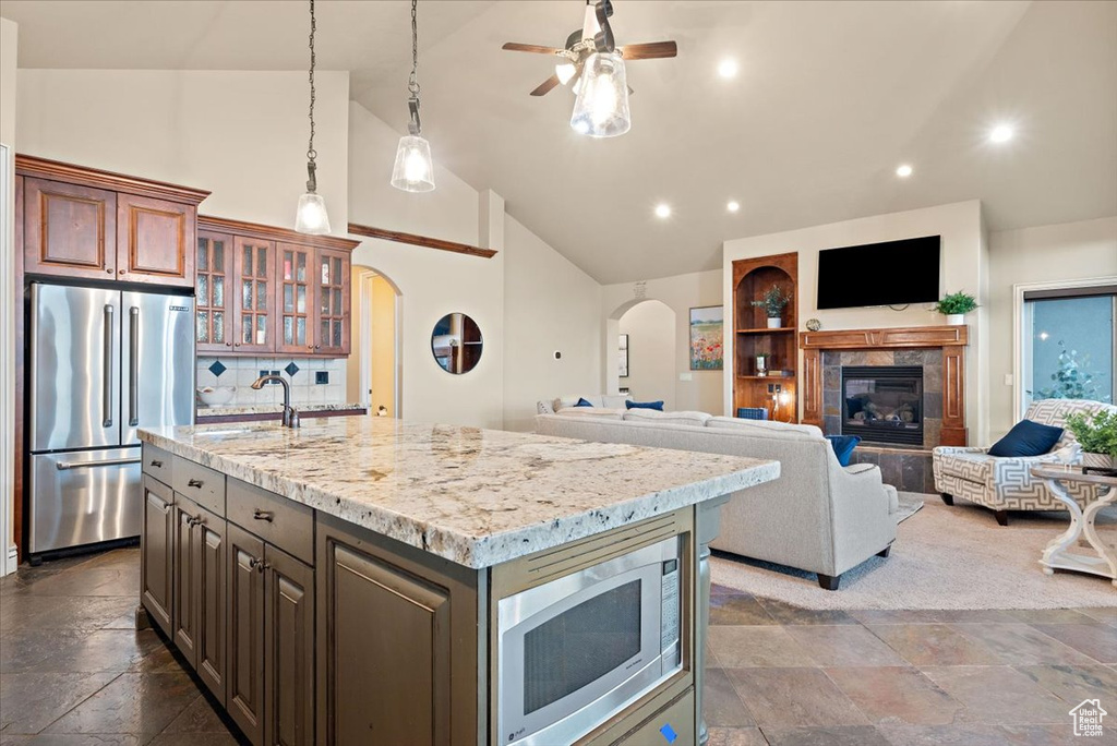 Kitchen with a center island with sink, appliances with stainless steel finishes, a tiled fireplace, sink, and dark tile flooring