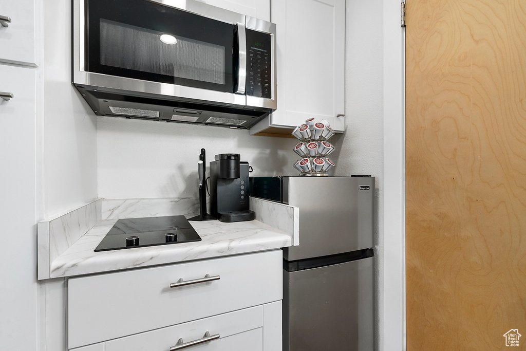 Kitchen featuring light stone countertops, stainless steel appliances, and white cabinetry