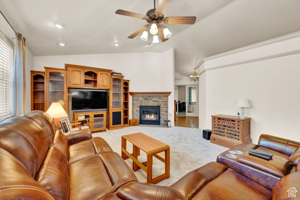 Carpeted living room featuring a stone fireplace, ceiling fan, and lofted ceiling