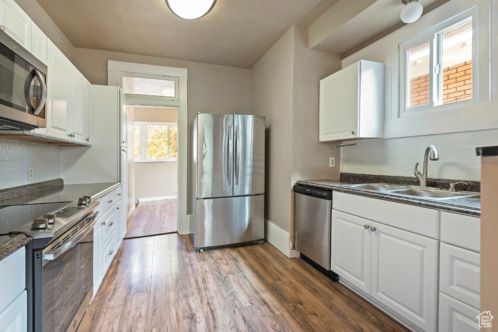 Kitchen with stainless steel appliances, white cabinets, sink, and wood-type flooring